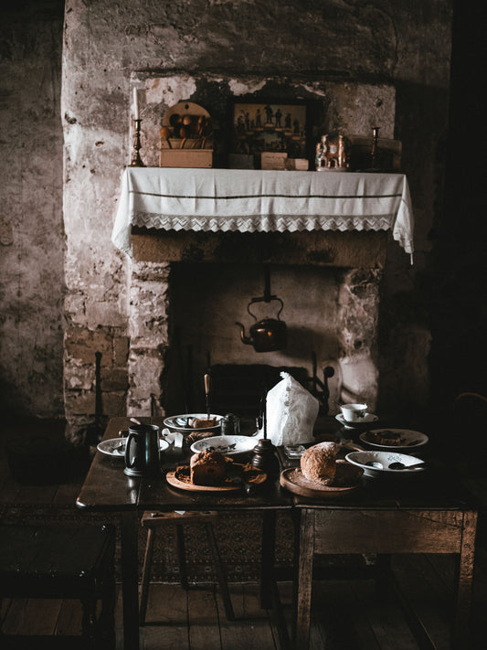 Dark rustic dining room with an old stone fireplace, wooden table, and vintage tableware
